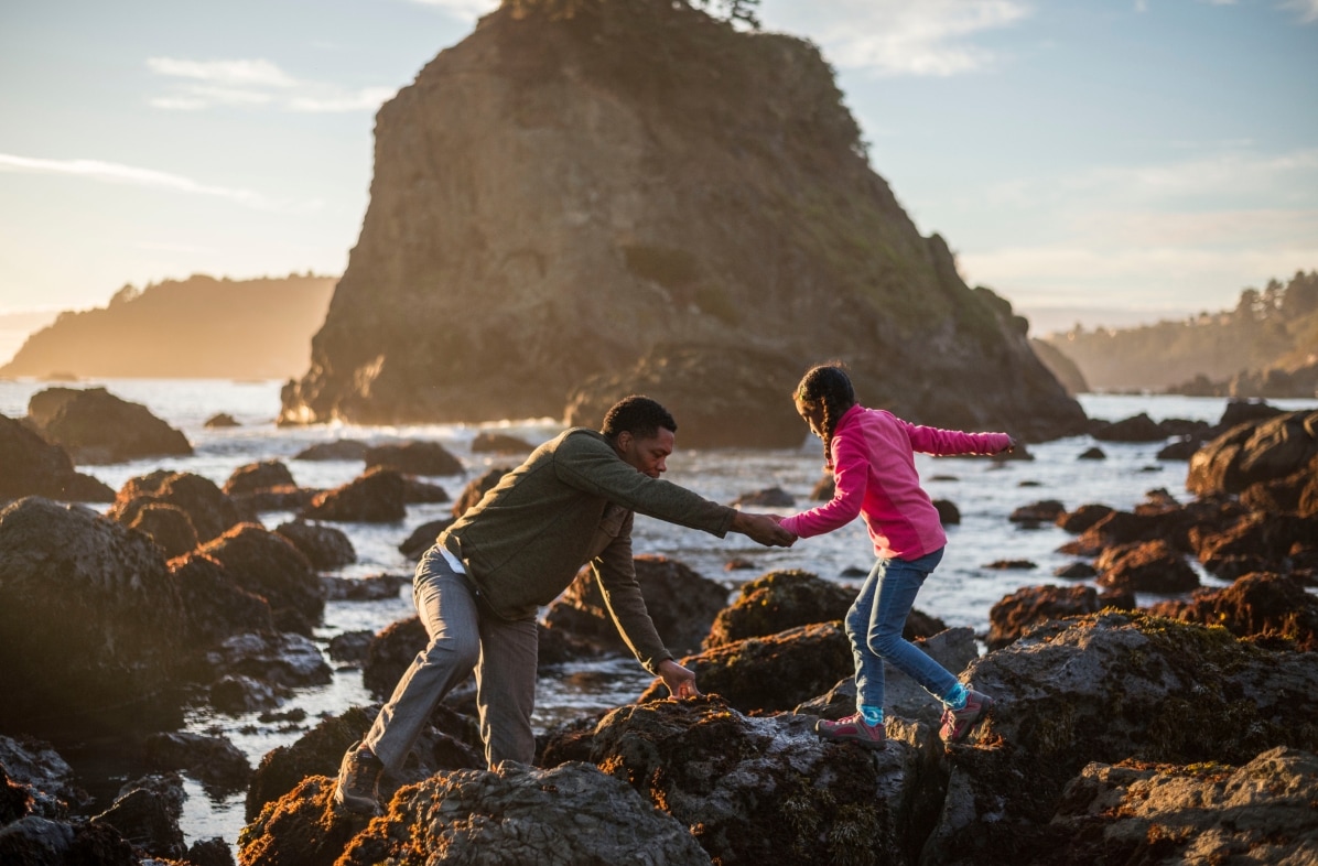 A father and daughter hike through rocky tidepools near an ocean