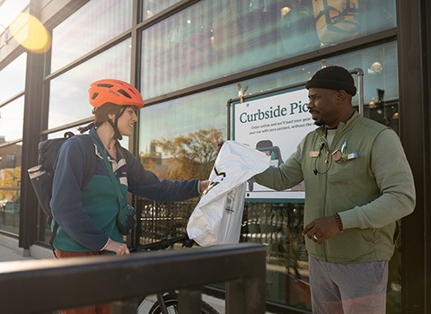 An REI customer on a bike outside of and REI store being handed an online order from a co-op employee.