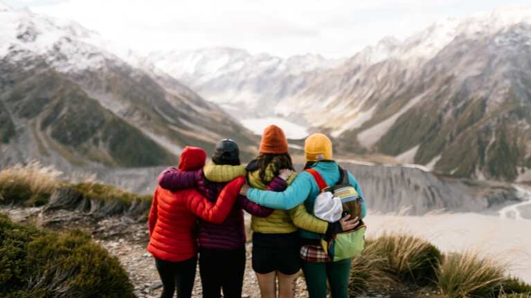 Group of four people embrace looking out over an alpine lake