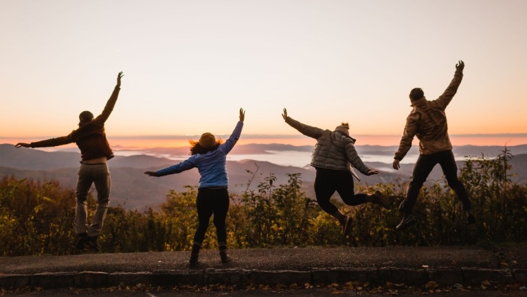 Group of four people jump for joy overlooking a lake