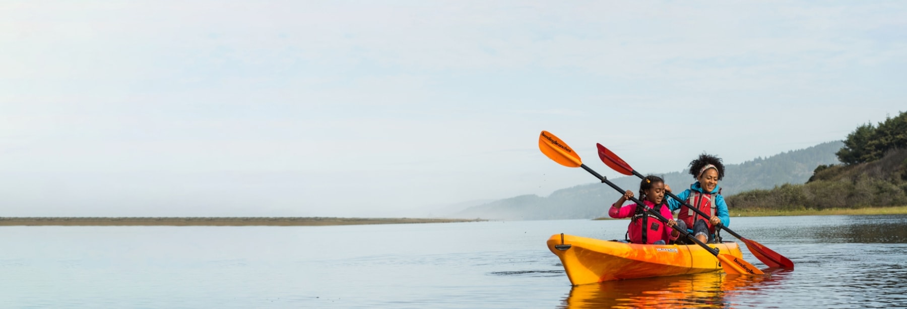 A mother and daughter smile while kayaking through calm water