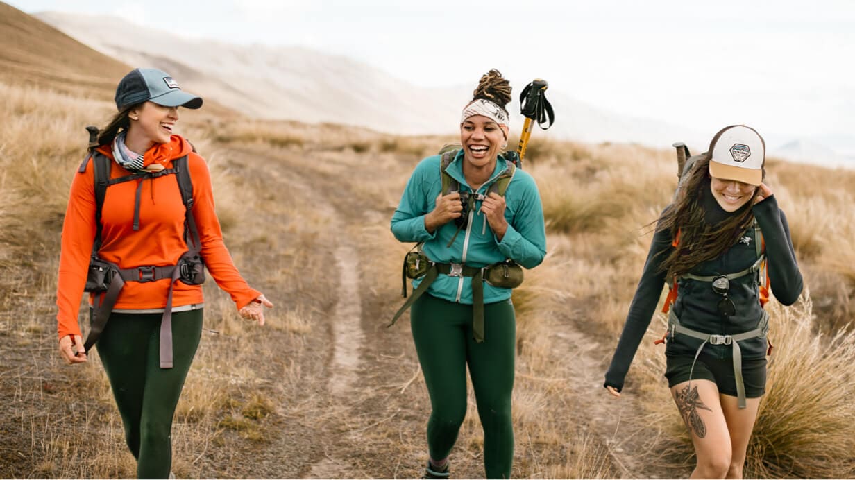 Three hikers laugh while hiking a grassy trail on New Zealand's south island.