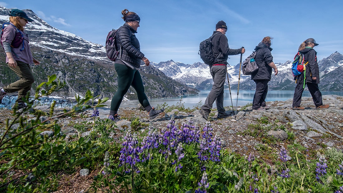 hikers walking in a line along a mountain that is above a lake