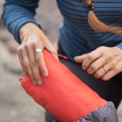 A person wearing a long-sleeved shirt and leggings places a small pouch containing an REI Co-op brand Flash Insulated Jacket into a day pack.