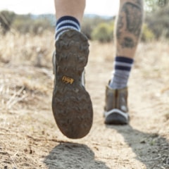 Close up of the tread on the bottom of an REI Co-op hiking boot, worn by a hiker on a dusty trail