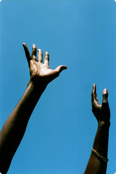 Two hands raised in the air against a clear blue sky.