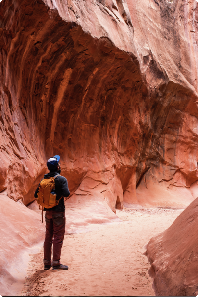 A hiker walks through the bottom of a reddened canyon.