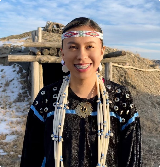 A person smiles in front of a partially snow-covered hill.