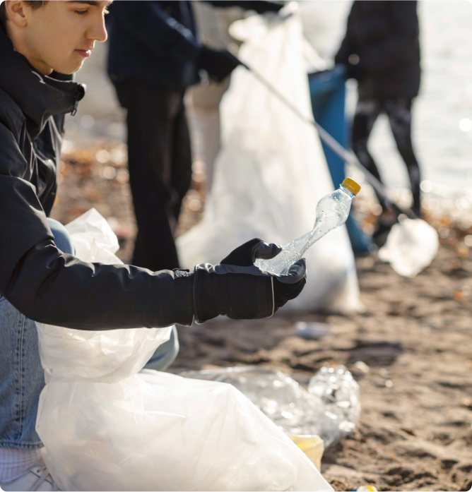 A person picks up a plastic bottle on a sandy beach.