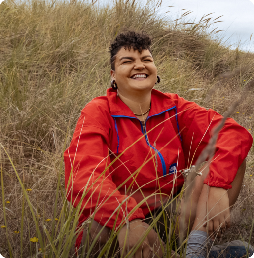 A person sits in grass next to a beach.