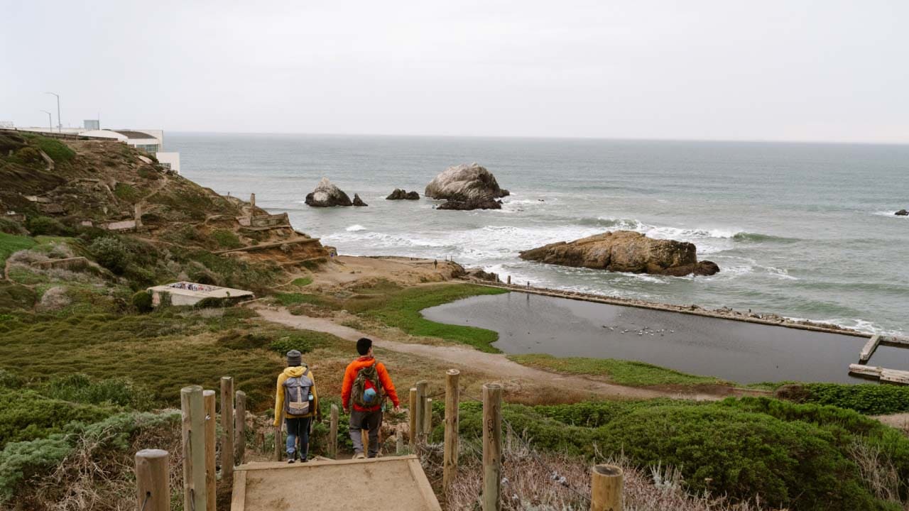 two people walking down a staircase to the beach on a gray day