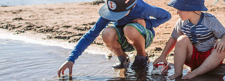 Two kids kneeling down by lake picking up rocks