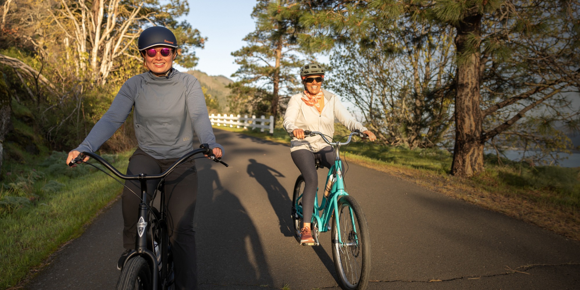 Two smiling cyclists ride on a bike trail