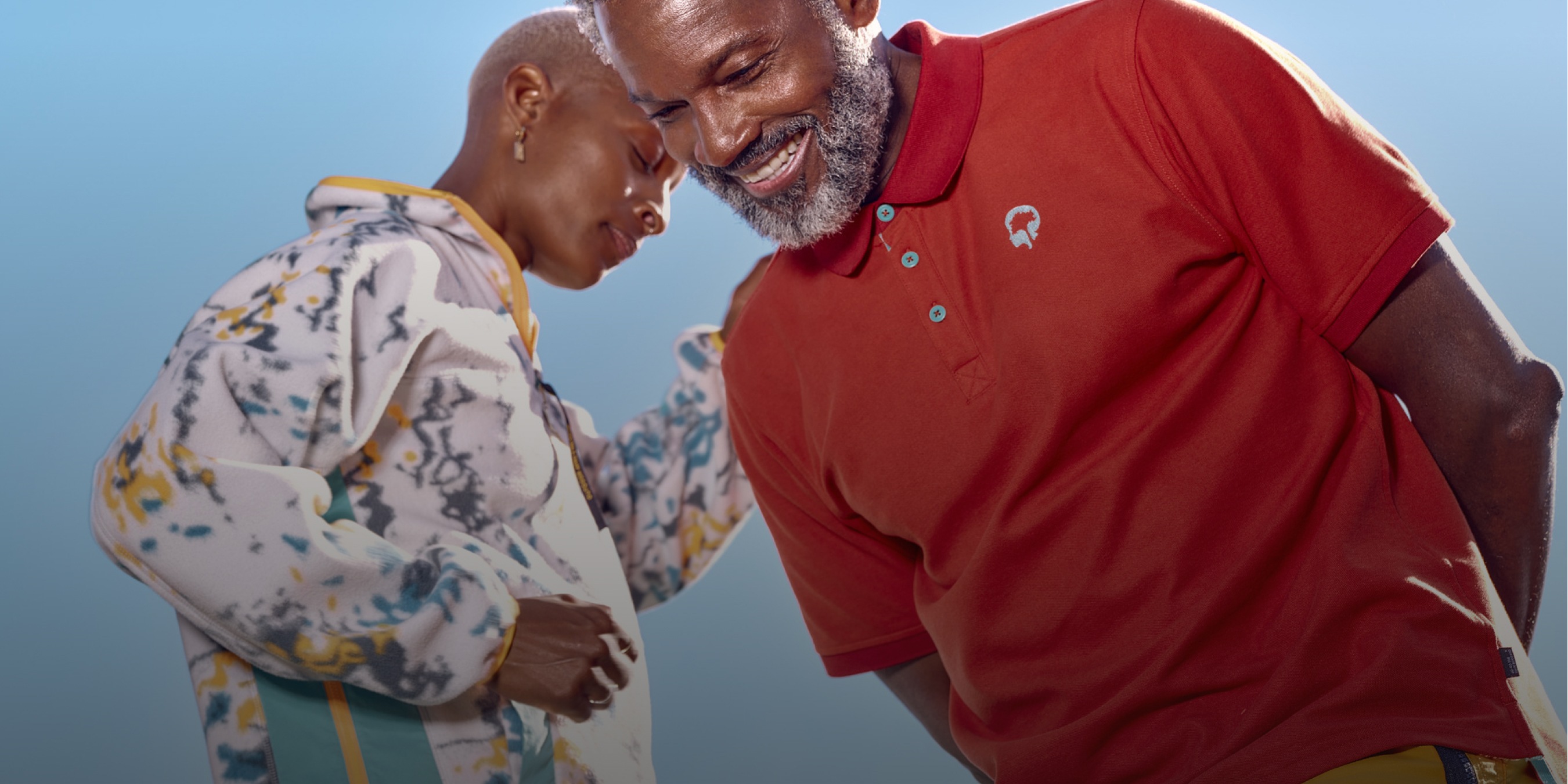 Two people wearing Outdoor Afro apparel laugh against the backdrop of a blue sky