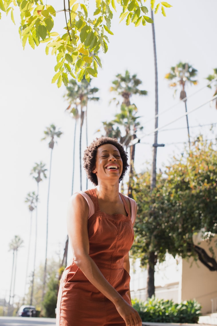 A person smiling outside with palm trees in the background.