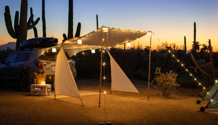 A desert campsite with a vehicle shelter and string lights.