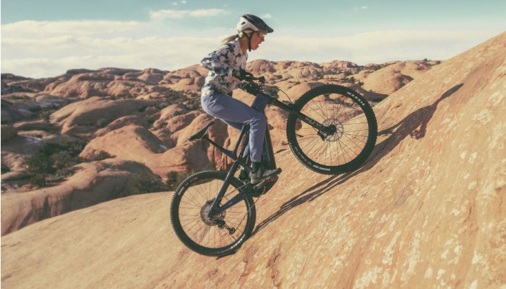 A cyclist riding the Cannondale Moterra Neo electric mountain bike in a dry, hilly terrain.