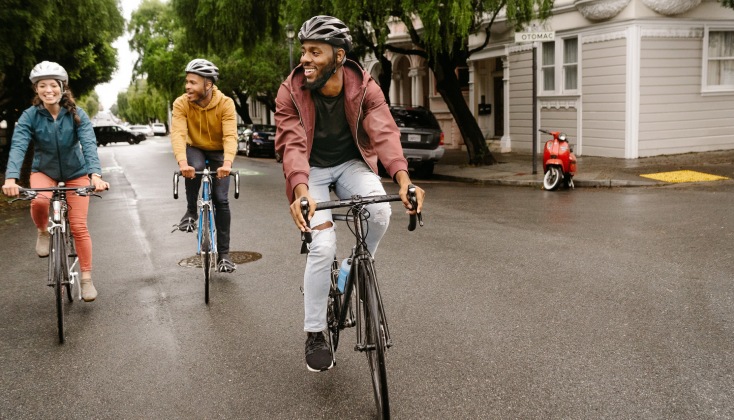 Three cyclists smiling and riding on a tree-lined residential street.