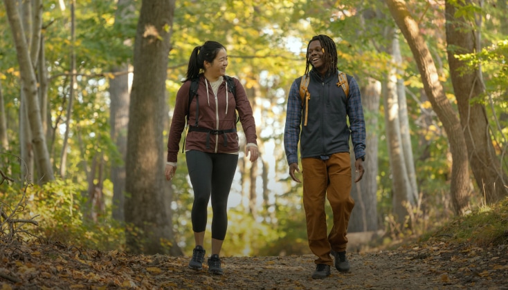 Two hikers walk down a tree-lined path.