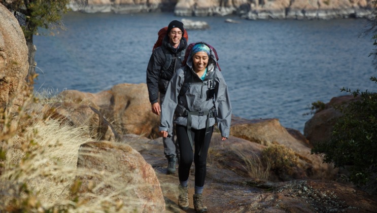 Two smiling hikers on a trail near water.