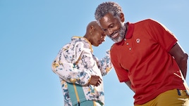 Two people wearing Outdoor Afro apparel laugh against the backdrop of a blue sky