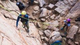 At the wall's base, a climber belays another on the face far above.