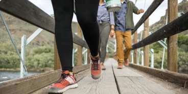 Three friends walk across a wooden bridge in the mountains.
