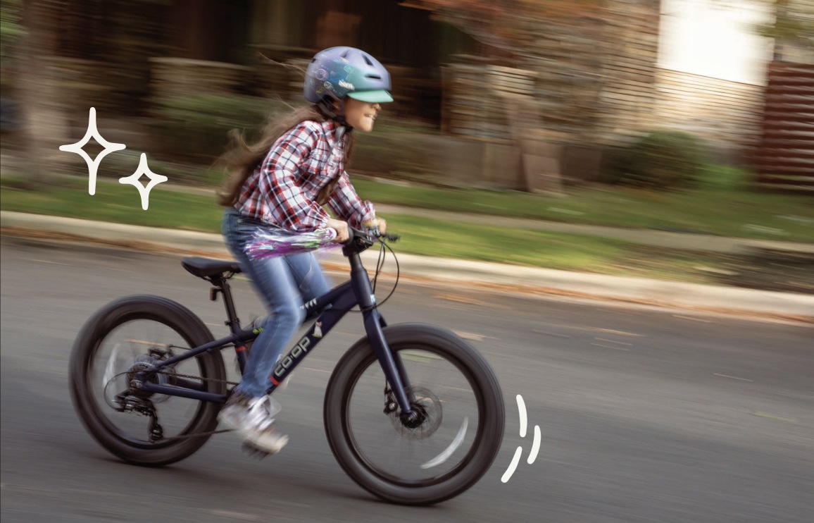 A child pedals fast on a bike while wearing a helmet.