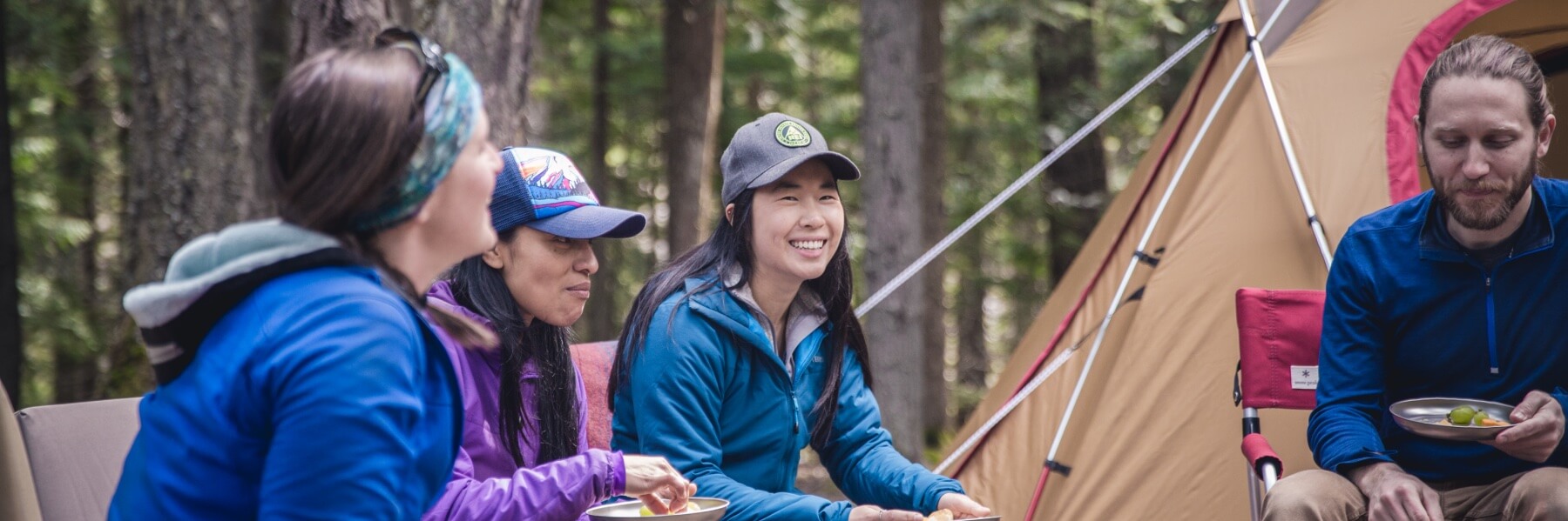 a couple of friends dote on a cute dog while chatting in front of their tent