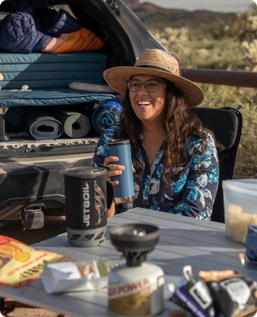 A camper sits at a table drinking from a thermos.