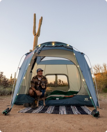 A camper and dog sit inside their tent at a desert campsite.