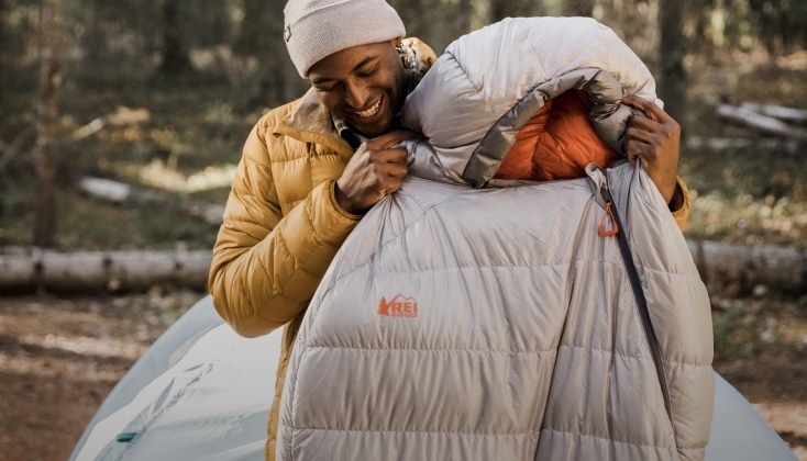 A man holds up a mummy sleeping bag