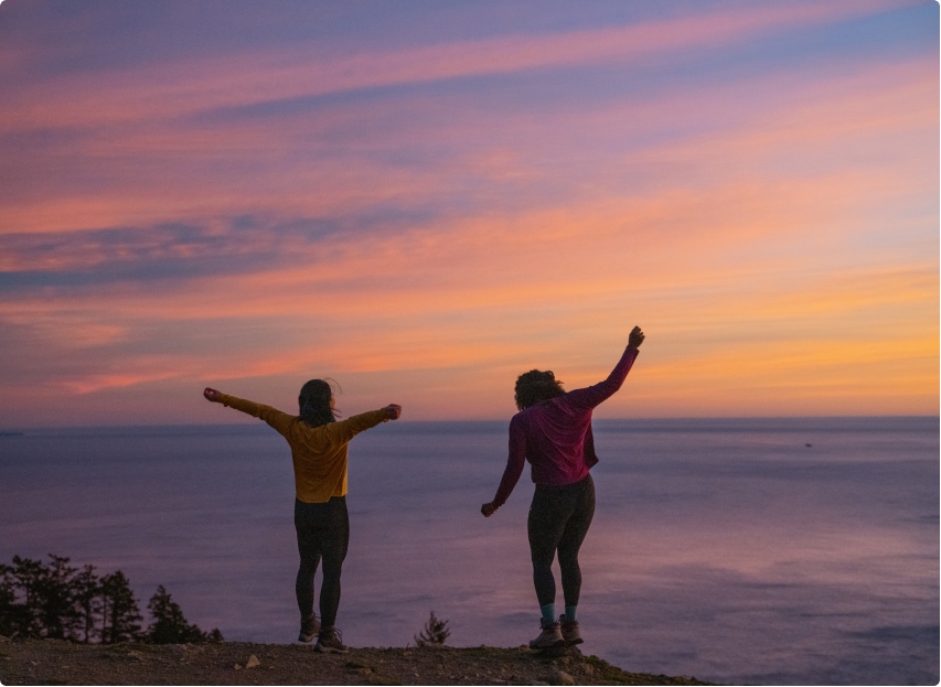 Two people standing in the breeze, looking out at the sunset over the ocean.