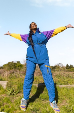 A person wearing Outdoor Afro Inc. plus R E I Co-op clothing, with arms outstretched in the sun.