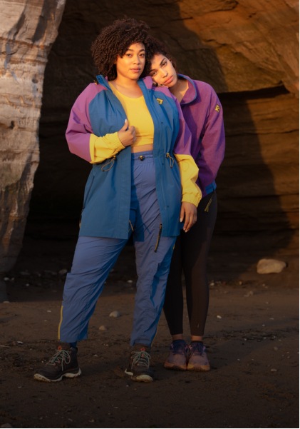 Two people looking at the camera and wearing the Outdoor Afro Inc. plus R E I Co-op collection, in front of a red rock cliff.
