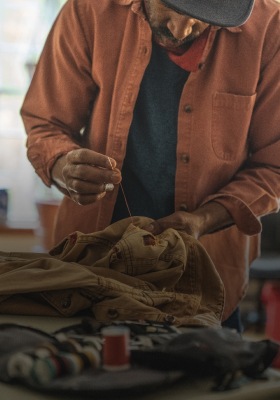 A tight shot of a craftsperson hand stitching something on a mustard yellow garment.