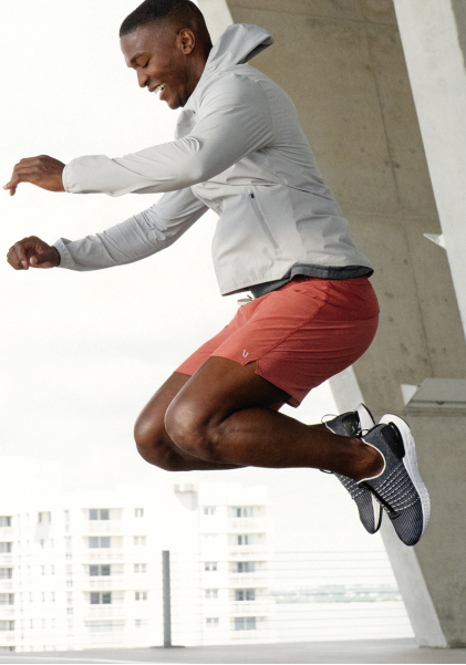 A smiling person in athletic apparel jumps during a workout