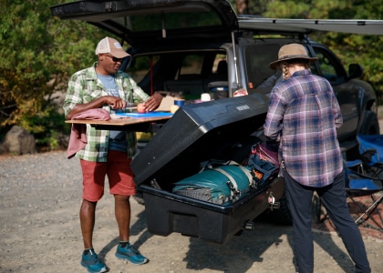A camper reaches into a Yakima roof box while another camper looks on.