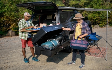 A camper reaches into a Yakima roof box while another camper looks on.