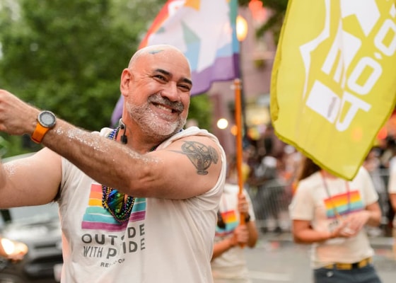 A group of marchers wave flags at a Pride parade.