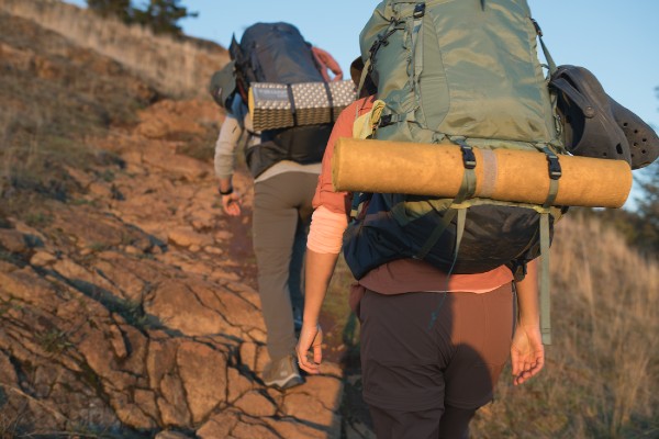 Setting out on a multi day hike, two friends ascend a rocky northwest island trail at dusk.