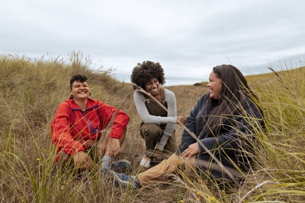 In a grassy field under billowy skies, three hikers share some laughs.