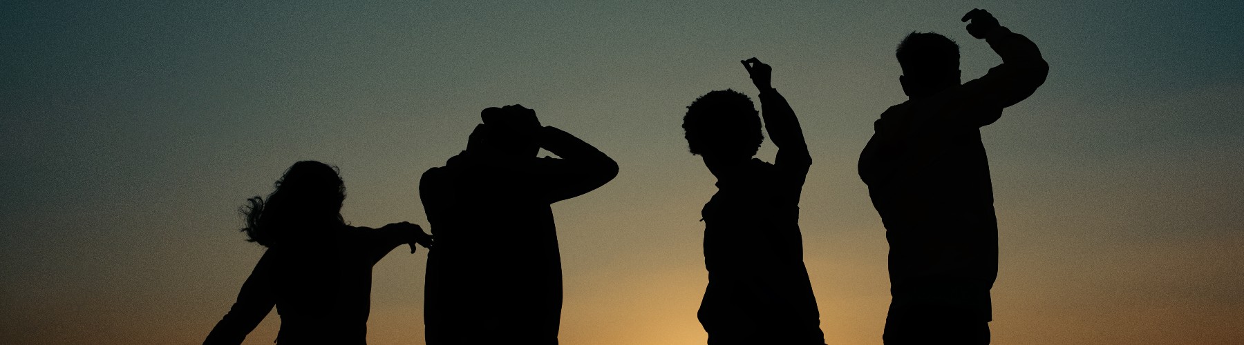 Silhouetted as shadows against the orange and blues of a fading sunset, four friends dance to nature's music.