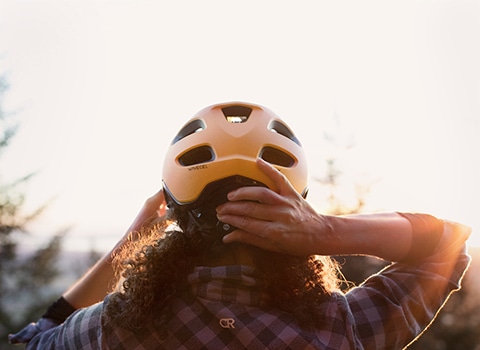 A Black cyclist adjusting her helmet while riding at sunset.