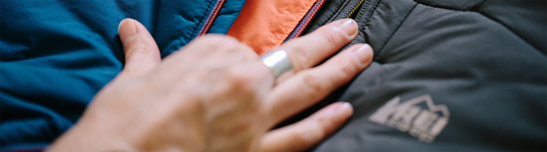 A hand holding several REI jackets together to compare color.