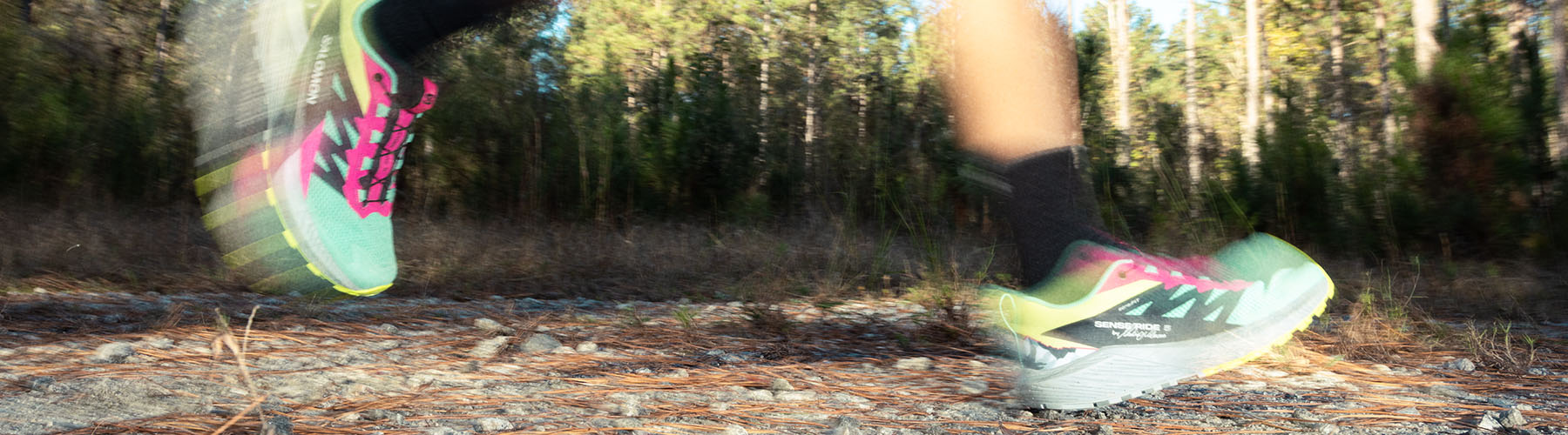 Feet of a runner mid stride on a trail in the woods.