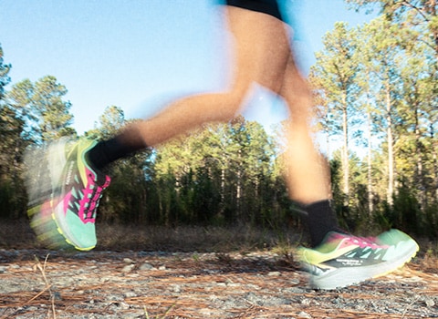 Feet of a runner mid stride on a trail in the woods.