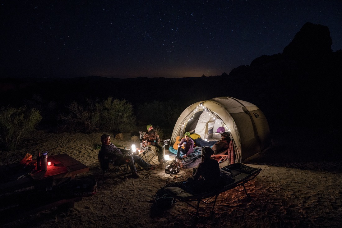 People sitting outside a tent with twinkle lights at night.