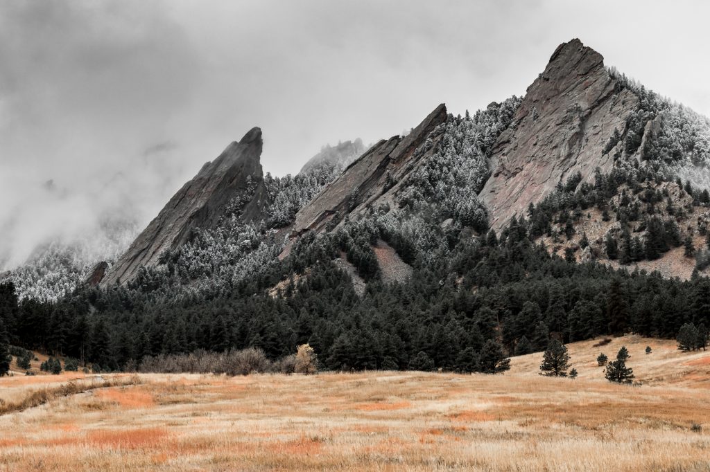 A light dusting of snow drapes the rocky Flatirons and surrounding trees.