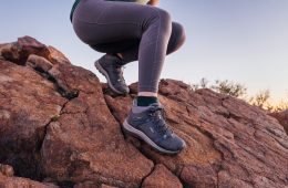 Women's legs, in grey leggings, descending a rock face with hiking boots on.